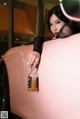 A woman leaning on the hood of a pink car holding a bottle of whiskey.