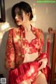 A woman in a red and gold chinese dress sitting on a chair.